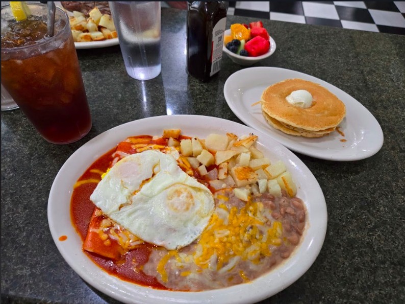 Red enchiladas with fried egg, beans, potatoes and a side of pancakes